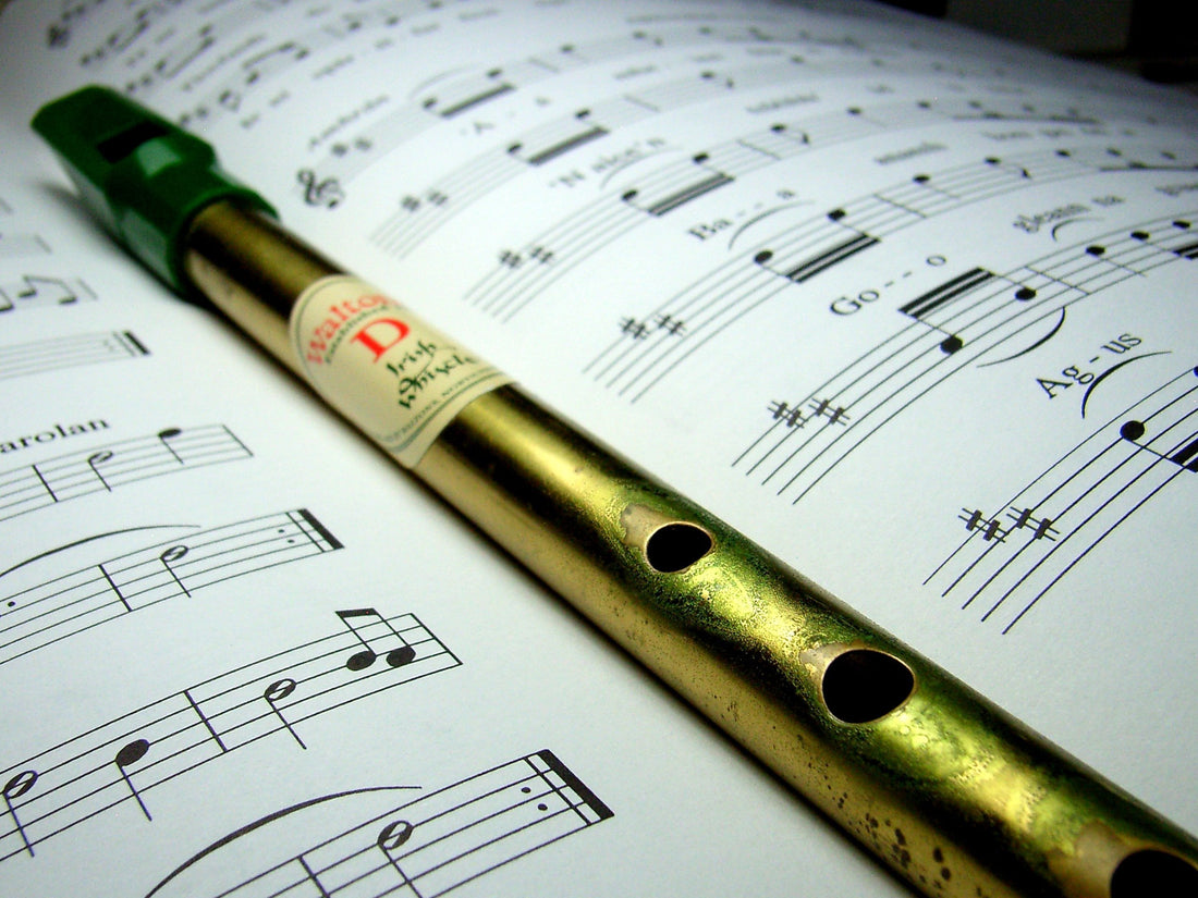 A brass tin whistle rests in the fold of a music book