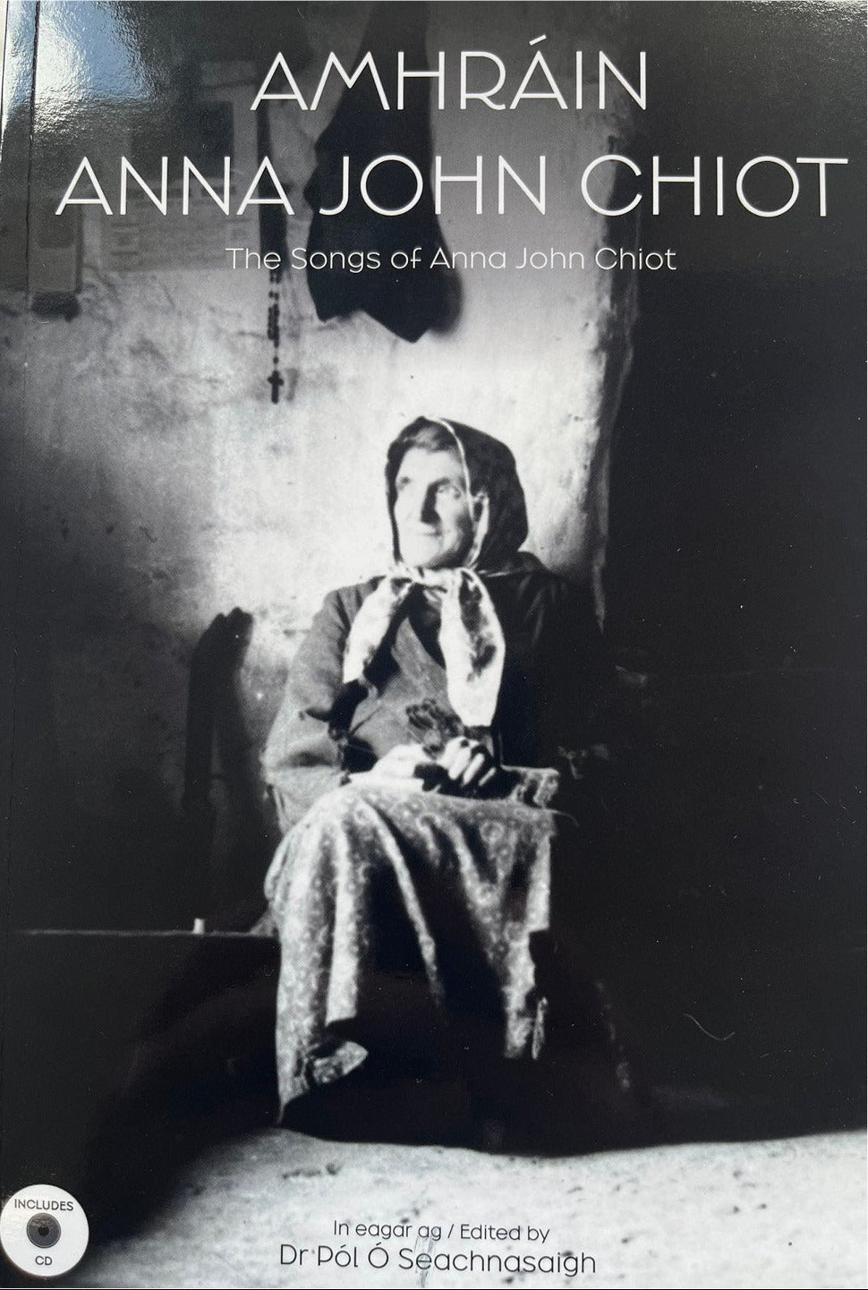 Black and white photo of a woman sitting in a cottage. The title is Amhrain Anna John Chiot, The Songs of Anna John Chiot