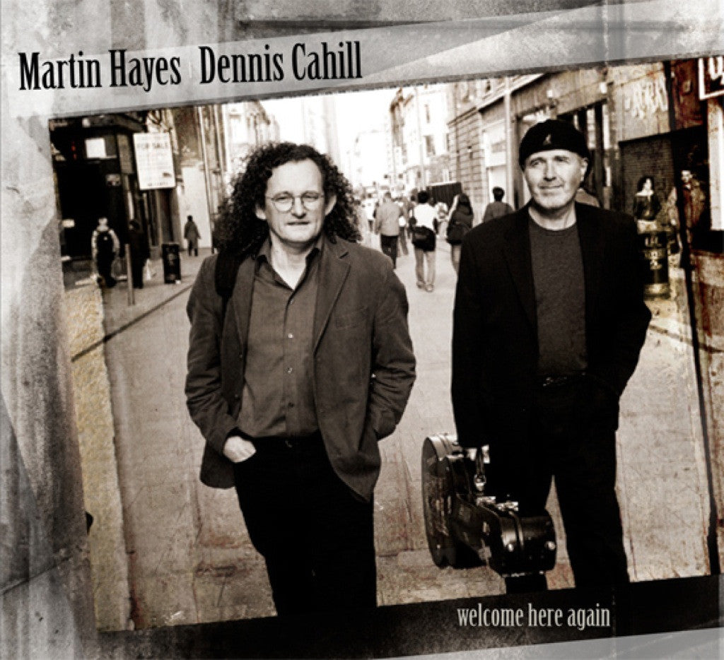 A black and white photo of a man walking down a city street, with another man carrying a guitar case. The title reads Martin Hayes Dennis Cahill Welcome Here Again.