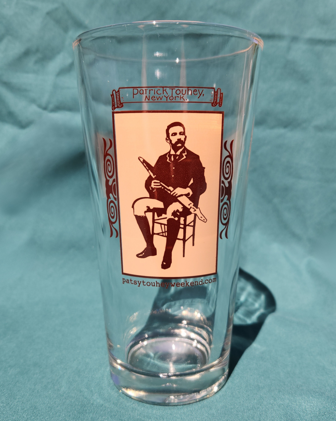 Clear glass with a printed design of a man playing uilleann pipes on a green fabric background